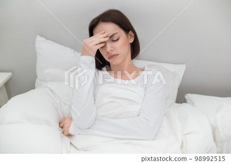 Unhappy young woman sitting in bed, touching forehead 98992515