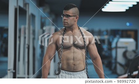 Muscular Arab in the gym walks with a metal chain after a workout. 98992720