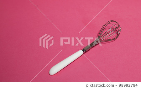 Manual metal whisk for whipping cream for baking desserts on a pink background. Baking concept. 98992784