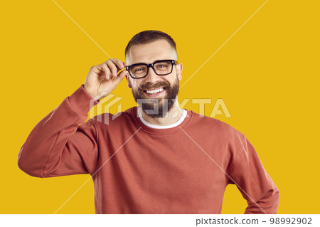 Happy smiling young man in glasses and sweatshirt standing isolated on yellow background Happy smiling young man in glasses and sweatshirt standing isolated on yellow background 98992902