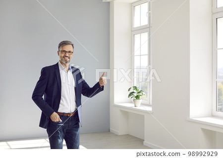 Joyful male realtor or real estate agent showing thumb up while standing in new building. 98992929
