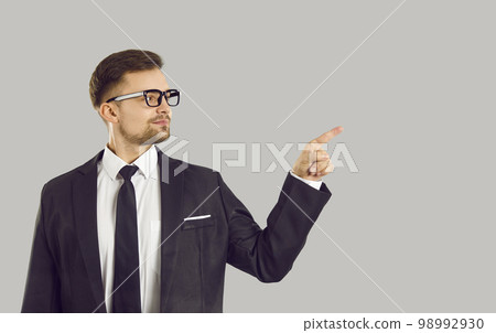 Confident handsome young businessman pointing finger at content or copy space on gray background. Confident handsome young businessman pointing finger at content or copy space on gray background. 98992930