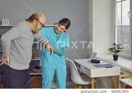 Elderly man with glasses, walking holding the small of his back with caring nurse. Elderly man with glasses, walking holding the small of his back with caring nurse. 98992965
