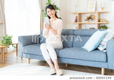 Middle woman operating a smartphone in the room 98993199