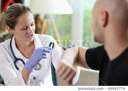 Gloved woman dermatologist examining skin of bald patient with magnifying glass. 98993774