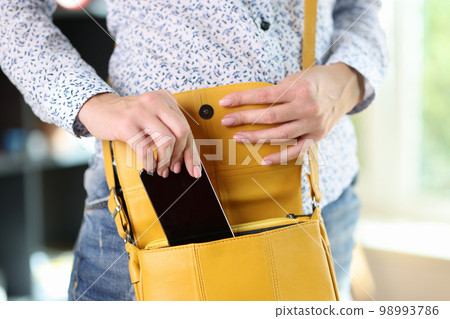 Woman in casual clothes hides smartphone in yellow bag. Woman in casual clothes hides smartphone in yellow bag. 98993786
