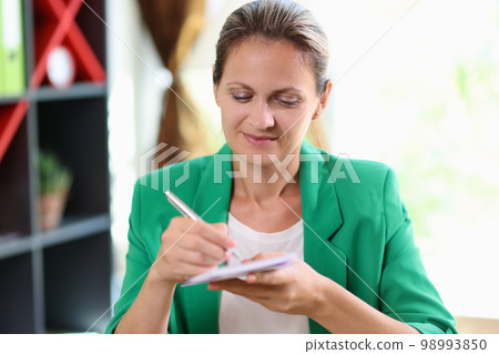 Satisfied business woman smiling and writing notes in her notepad in the office. 98993850
