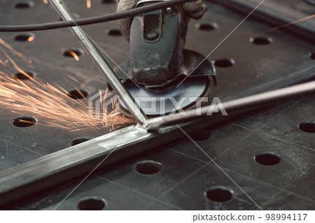 Worker in metal factory grinding workpiece with sparks flying 98994117