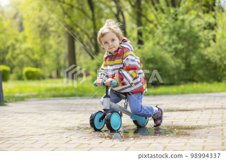 Active blond boy riding balance bike or run bike outdoor park 98994337