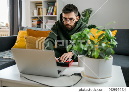 Man music producer or arranger using laptop and midi keyboard and other audio equipment to create music at home studio. Beat making and arranging audio content and composing song concept Man music producer or arranger using laptop and midi keyboard and other audio equipment to create music at home studio. Beat making and arranging audio content and composing song concept 98994684