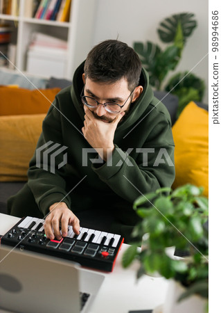Man music producer or arranger using laptop and midi keyboard and other audio equipment to create music at home studio. Beat making and arranging audio content and composing song concept Man music producer or arranger using laptop and midi keyboard and other audio equipment to create music at home studio. Beat making and arranging audio content and composing song concept 98994686