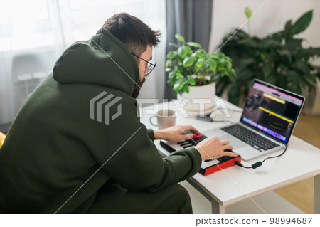 Man music producer or arranger using laptop and midi keyboard and other audio equipment to create music at home studio. Beat making and arranging audio content and composing song concept 98994687