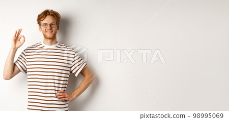 Confident smiling man with red hair assuring you, showing OK sign, guarantee quality, recommending something good, standing over white background Confident smiling man with red hair assuring you, showing OK sign, guarantee quality, recommending something good, standing over white background 98995069