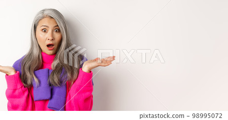 Close up of shocked asian mom staring at camera, spread hands sideways and gasping at camera confused, standing over white background Close up of shocked asian mom staring at camera, spread hands sideways and gasping at camera confused, standing over white background 98995072