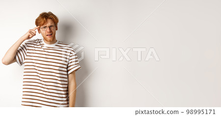 Annoyed young man with red hair scolding person for being stupid, pointing at head and staring at camera, white background Annoyed young man with red hair scolding person for being stupid, pointing at head and staring at camera, white background 98995171