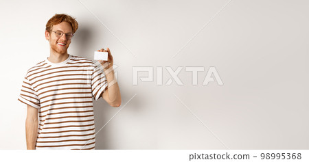 Shopping and finance concept. Cheerful redhead male student in glasses showing plastic credit card and looking satisfied, standing over white background Shopping and finance concept. Cheerful redhead male student in glasses showing plastic credit card and looking satisfied, standing over white background 98995368