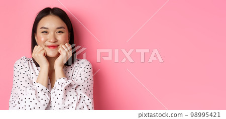 Beauty and lifestyle concept. Close-up of adorable asian woman showing puffy cheeks, smiling and looking happy, standing over pink background Beauty and lifestyle concept. Close-up of adorable asian woman showing puffy cheeks, smiling and looking happy, standing over pink background 98995421