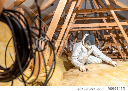 man insulates the roof and ceiling of the house with glass wool man insulates the roof and ceiling of the house with glass wool 98995435