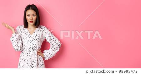 Careless asian woman raising hand and shrugging, staring at camera unbothered and questioned, so what gesture, standing over pink background Careless asian woman raising hand and shrugging, staring at camera unbothered and questioned, so what gesture, standing over pink background 98995472