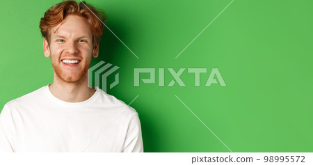 Emotions and fashion concept. Happy young man with red hair and beard, smiling and laughing at camera, standing over green background Emotions and fashion concept. Happy young man with red hair and beard, smiling and laughing at camera, standing over green background 98995572