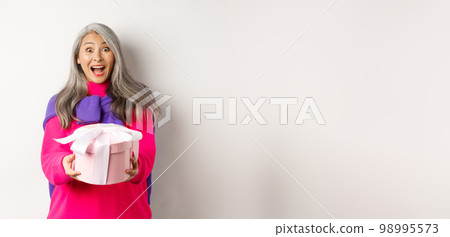 Surprised senior asian woman receiving valentines day gift and smiling amazed, holding present box, standing over white background Surprised senior asian woman receiving valentines day gift and smiling amazed, holding present box, standing over white background 98995573