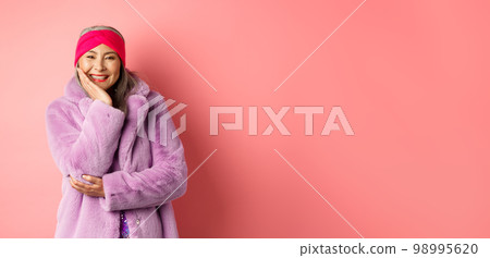 Fashion and shopping. Beautiful and romantic asian mature woman looking caring and heartfelt at camera, smiling happy, standing over pink background 98995620