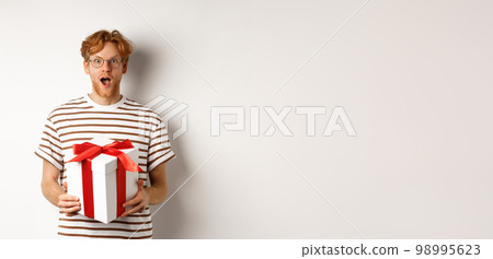 Valentines day and holidays concept. Surprised redhead boyfriend in glasses looking grateful at camera, receive big present in box, standing over white background 98995623