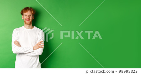 Young ambitious man with red hair standing over green background, holding hands crossed on chest and smiling 98995822