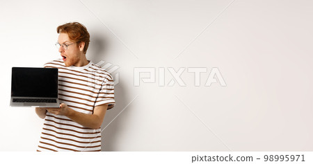 Young redhead man look impressed, showing laptop empty screen with logo banner. Guy in glasses checking out online advertisement on computer, white background 98995971