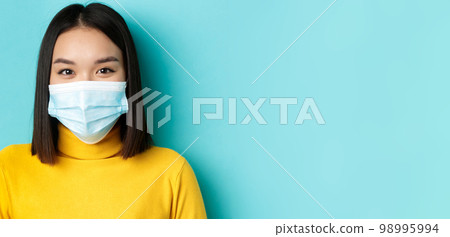 Covid-19, social distancing and pandemic concept. Close up of young asian woman with short dark hair, wearing medical mask and smiling with eyes, looking hopeful at camera 98995994