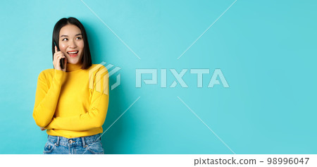 Stylish korean woman calling on phone, talking on smartphone and looking happy at upper right corner, smiling carefree, standing in relaxed pose over blue background Stylish korean woman calling on phone, talking on smartphone and looking happy at upper right corner, smiling carefree, standing in relaxed pose over blue background 98996047