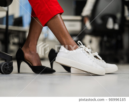 African woman changing from high heels to sneakers in the office. Tired legs.  98996185
