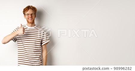 Smiling young male student with red hair and bristle, showing thumb-up and looking satisfied, leave positive feedback, recommending promo, white background Smiling young male student with red hair and bristle, showing thumb-up and looking satisfied, leave positive feedback, recommending promo, white background 98996282