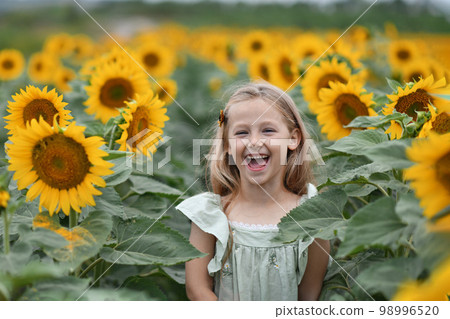 A girl in a dress enjoys life in a field with the sunflowers A girl in a dress enjoys life in a field with the sunflowers 98996520