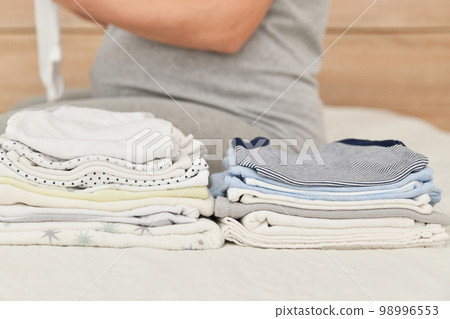 Pile of baby clothes and pregnant woman on a bed Pile of baby clothes and pregnant woman on a bed 98996553
