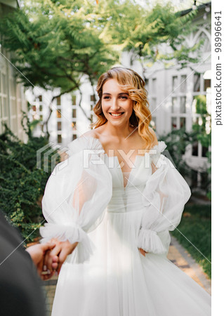 the bride by the hand with the groom walks through the garden. the bride by the hand with the groom walks through the garden. 98996641