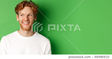 Headshot of happy redhead man with beard wearing white long sleeve, looking left at copy space and smiling, standing over green background Headshot of happy redhead man with beard wearing white long sleeve, looking left at copy space and smiling, standing over green background 98996910