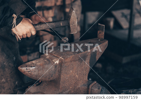 Blacksmith working metal with hammer and pincers on anvil in forge. Farrier strike iron in workshop. Metalworking. 98997159