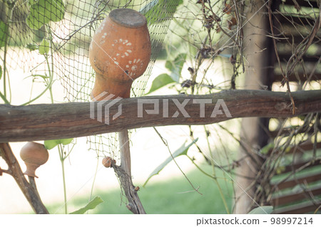 Old clay pot hanging upside down on wooden fence. Handmade antique ceramic vase outdoors. Rustic decor, crockery. 98997214