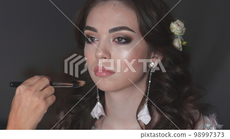 Girl make-up artist applies powder on the face of the model. 98997373