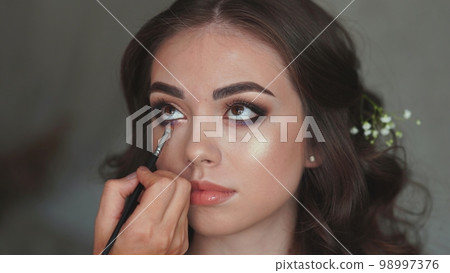 Makeup artist paints an eye for a model girl. Makeup artist paints an eye for a model girl. 98997376