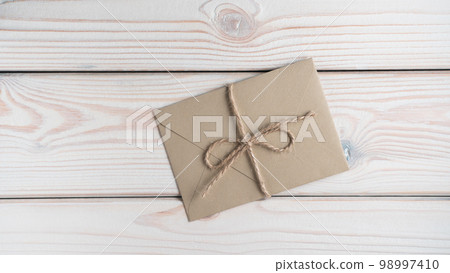 Top view of sealed closed brown craft envelope tied with string coarse twine on grey wooden table. Mailing, recycling. Top view of sealed closed brown craft envelope tied with string coarse twine on grey wooden table. Mailing, recycling. 98997410