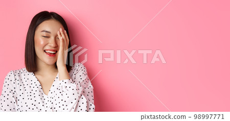 Beauty and lifestyle concept. Close-up of happy asian female laughing, looking happy and showing genuine emotions, standing over pink background Beauty and lifestyle concept. Close-up of happy asian female laughing, looking happy and showing genuine emotions, standing over pink background 98997771