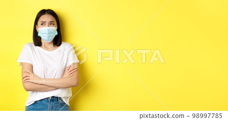 Covid, health care and pandemic concept. Asian woman in white t-shirt and medical mask cross arms on chest and looking up pensive and worried 98997785