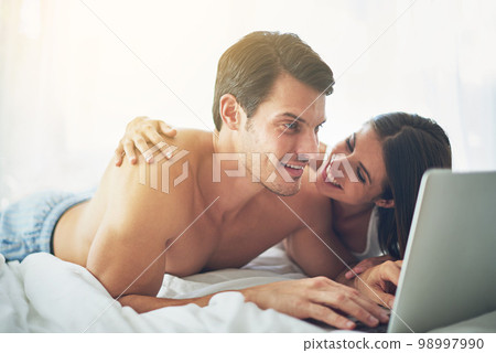 Couple with laptop, streaming and relax in home with technology, wifi and happy to chill together. Love, commitment and relationship with man and woman in bedroom with film website subscription 98997990