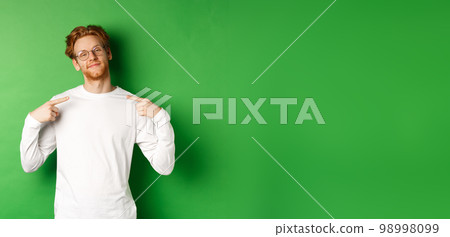 Confident and smug redhead man in glasses smiling, pointing at himself self-assured, standing over green background Confident and smug redhead man in glasses smiling, pointing at himself self-assured, standing over green background 98998099