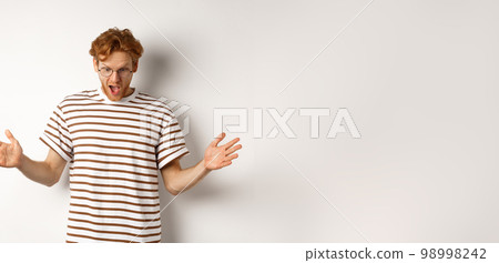 Impressed redhead man in glasses showing length of something big, demonstrate large size and looking amazed, standing over white background 98998242
