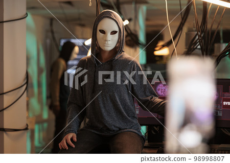 Cybercriminal calling victim and asking for ransom, threatening to expose important data from hacked server. Masked hacker committing internet fraud with live broadcast late at night. Cybercriminal calling victim and asking for ransom, threatening to expose important data from hacked server. Masked hacker committing internet fraud with live broadcast late at night. 98998807