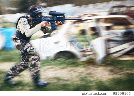 Paintball, aim and man with a gun for a game with blur motion at an outdoor arena or field. Challenge, competition and male soldier with a camouflage military outfit shooting a rifle on a battlefield 98999165