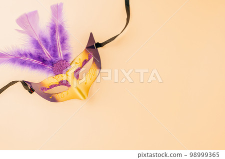 Happy Purim carnival decoration. Top view venetian ball mask with purple feather on pastel background, Jewish Purim and Mardi Gras in Hebrew, holiday background banner design, Masquerade party 98999365